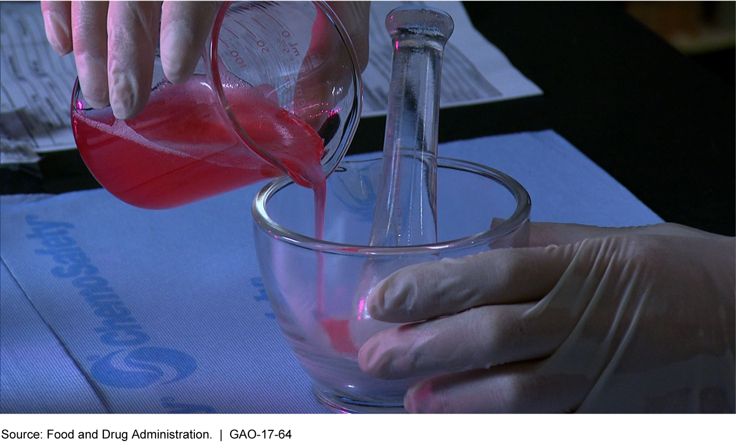Photo of hands in medical gloves pouring red liquid into a glass mortar and pestle.