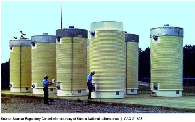 Two workers standing near several dry cask storage tanks