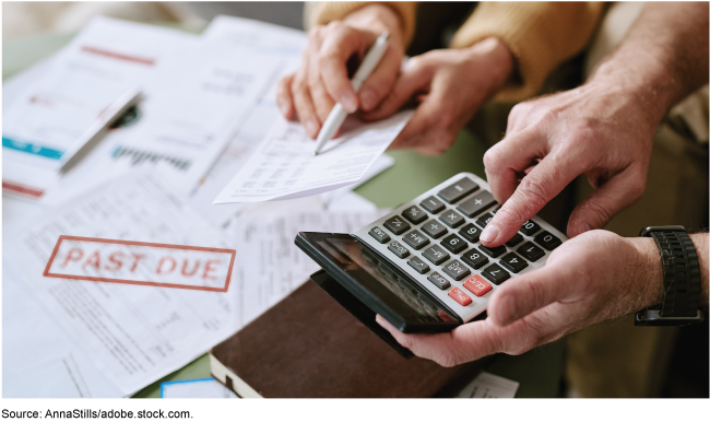 One person's hands hold a calculator, while another's hold a bill and a pen. A notice of a past due payment is on the table next to them. One person's hands hold a calculator, while another's hold a bill and a pen. A notice of a past due payment is on the table next to them.