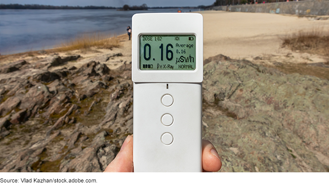 Photo showing someone holding up a device that detects radiation on a beach.