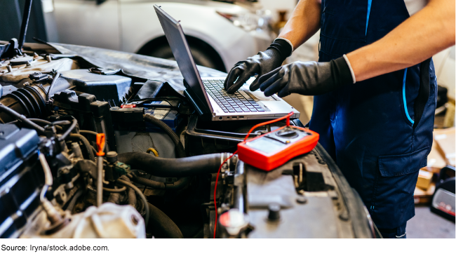 An auto mechanic using a laptop to work on a card with its hood raised