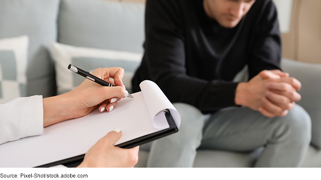 Stock image showing someone sitting on a couch across from a mental health care provider who is taking notes.