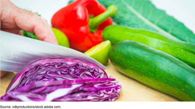 A person using a knife to cut various vegetables.