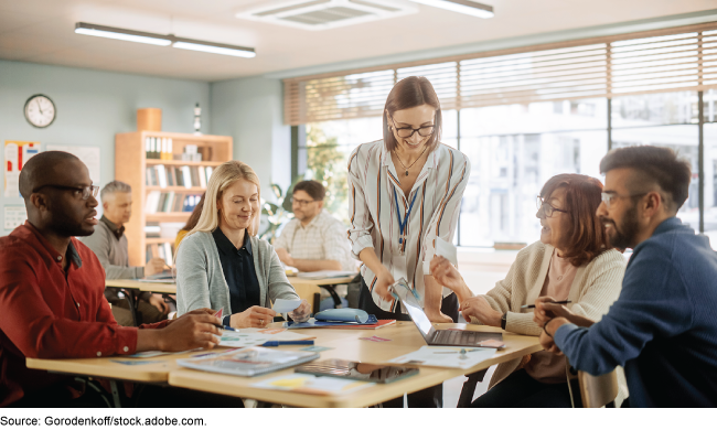 A group of people in a classroom talking while sitting in groups. A group of people in a classroom talking while sitting in groups.