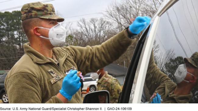 Soldier wearing medical gloves and a face mask stands facing a car door.