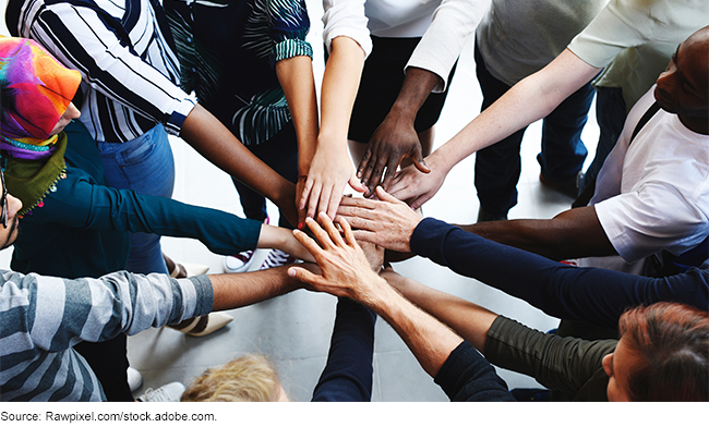 A diverse group of people in a huddle with their hands overlapping. 