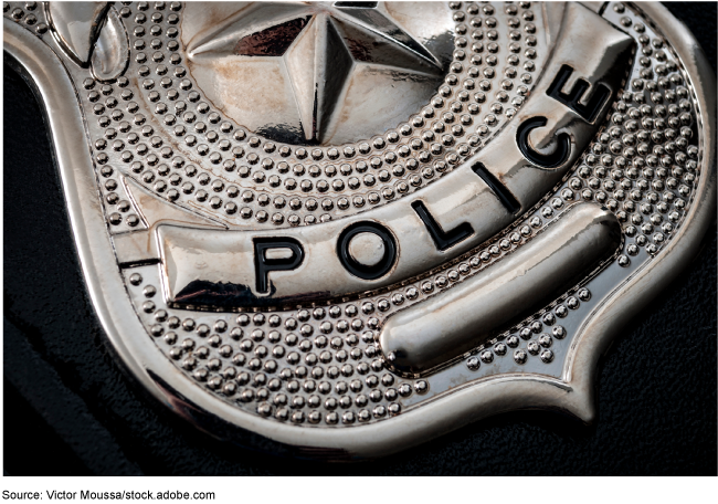 Close-up of a shiny, silver police badge against a black background. Close-up of a shiny, silver police badge against a black background.