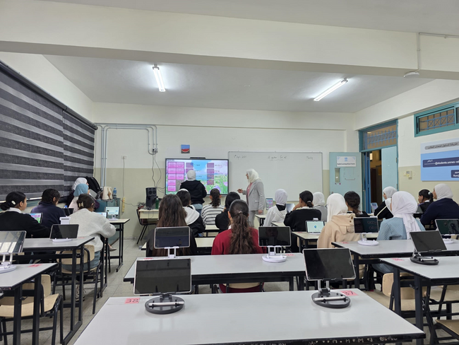 Teachers provide a lesson on an electronic board to a classroom full of Palestinian students.