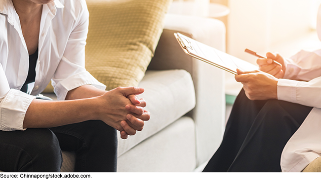 Photo showing the hands of two people sitting opposite one another, one holding a clipboard with a pen