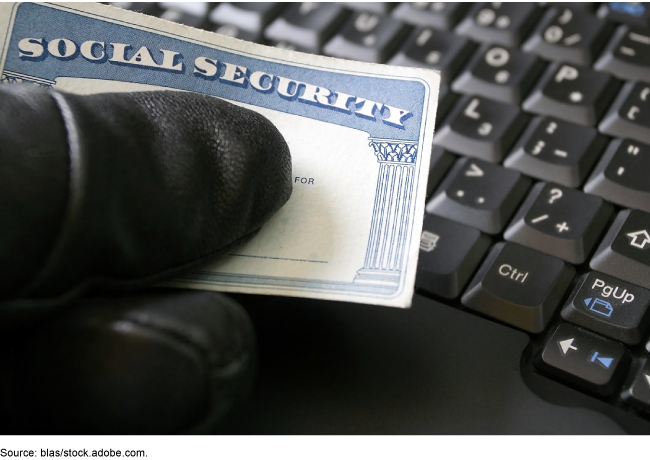 Gloved hand holding social security card above a keyboard.