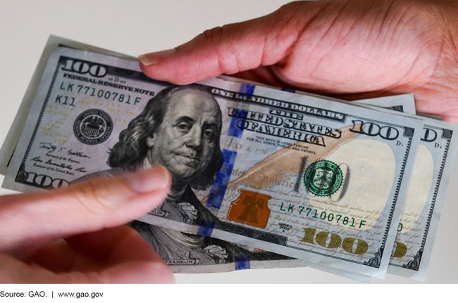 Photo of a person handing off $100 bills to another person.  