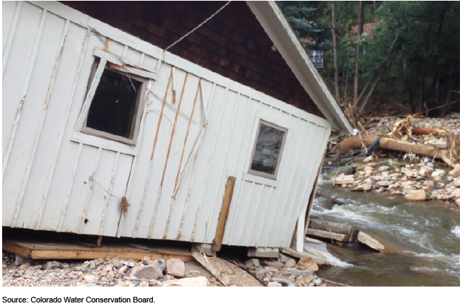 A damaged building with water flowing along the side of it.