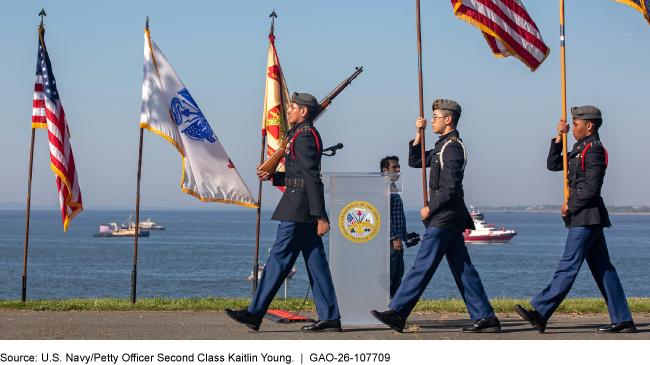JROTC cadets march with flags during Fleet Week with water in the background.