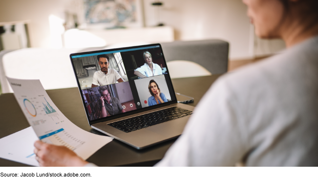 An image of an individual reading printed graphs while in front of a computer screen during a remote video meeting.