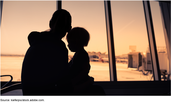 A woman with a young child sitting in her lap in an airport looking out at the passenger boarding bridges.