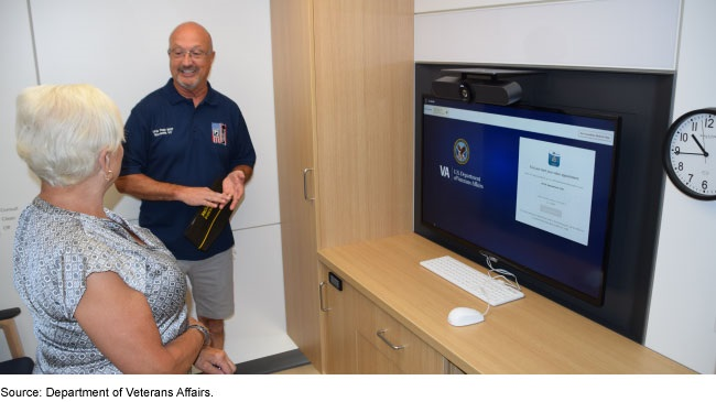 two people in conversation in front of a computer screen displaying VA information