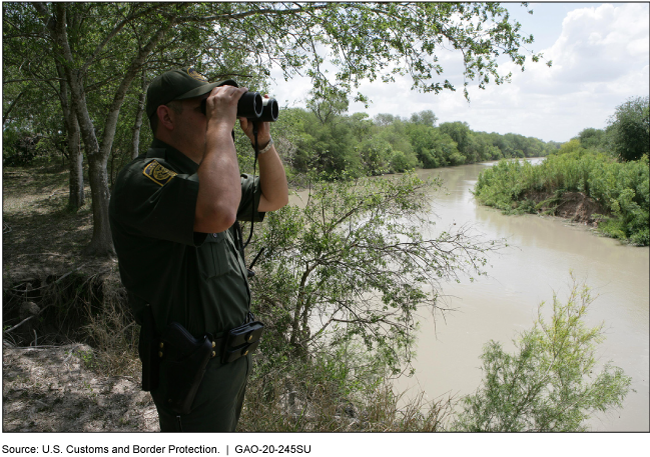 A uniformed agent with a pair of binoculars looks out over a creek