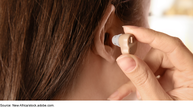 Close up showing someone placing a hearing aid in their ear. 