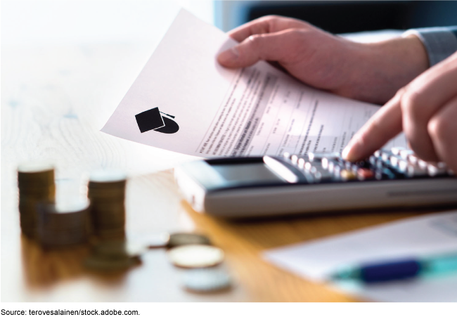 A person holding a student financial aid and using a calculator with coins stacked nearby