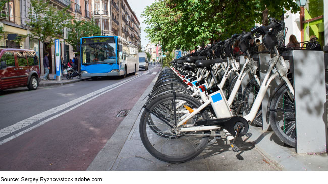 Image showing a line of city rental bicycles and a city bus in the background.