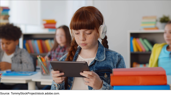 Portrait of preteen girl using headphones and a digital tablet in a classroom