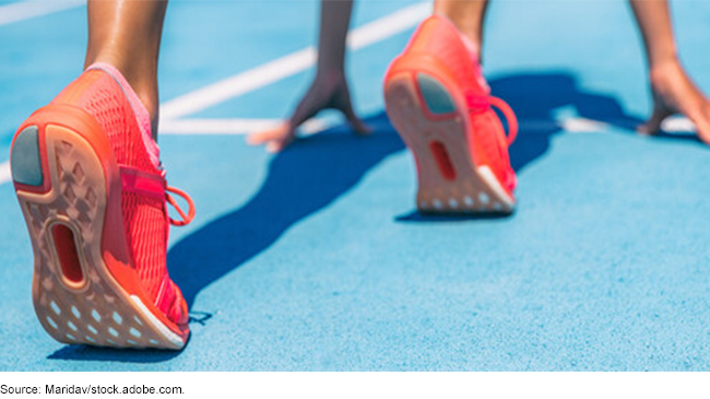 A runner posed to sprint. The runners' shoes and hands in position on the track. 