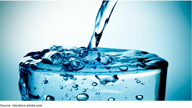 A glass with water being poured into it that is overflowing. A glass with water being poured into it that is overflowing.