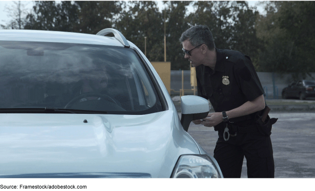 Police officer speaking to a driver of a vehicle through the open driver side window.