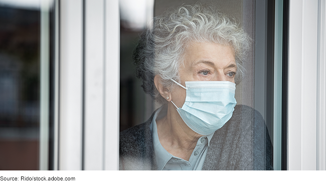 Elderly woman looking out a window with a medical mask covering her face.