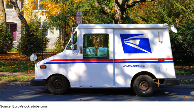 A U.S. Postal Service mail truck parked outside a home in autumn. 