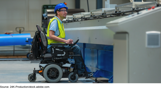 A man in an electric wheelchair, wearing safety glasses, a yellow vest and blue helmet in a factory. A man in an electric wheelchair, wearing safety glasses, a yellow vest and blue helmet in a factory.