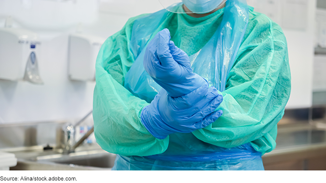 A person with medical surgery clothing on, securing the glove on their hand. A person with medical surgery clothing on, securing the glove on their hand.