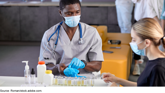 A man wearing medical attire at a table with glass bottles.