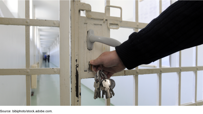 Hand inserting a key from a set of keys into a door at a prison.