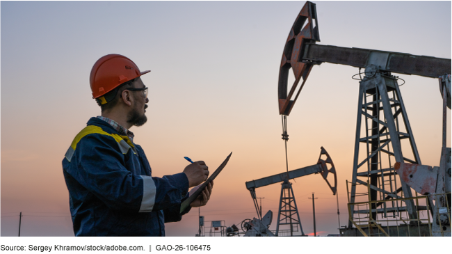 An oil and gas worker checks oil pump jacks and records data on a clipboard at sunset. An oil and gas worker checks oil pump jacks and records data on a clipboard at sunset.