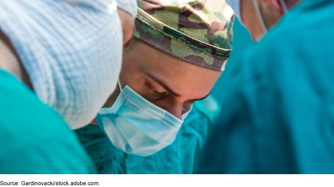 Military surgeons in scrubs and personal protective equipment operate in a hospital.