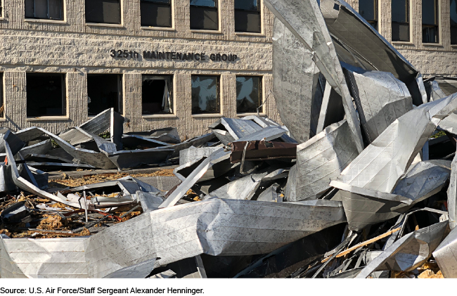 Piles of rubble and twisted metal sit in front of a building with broken windows. A sign on the building says 325th Maintenance Group. Piles of rubble and twisted metal sit in front of a building with broken windows. A sign on the building says 325th Maintenance Group.