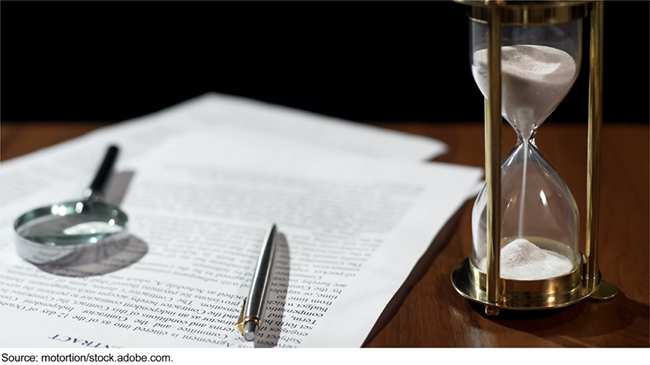 A contract with a pen and magnifying glass resting on top it and an hour glass next to it.