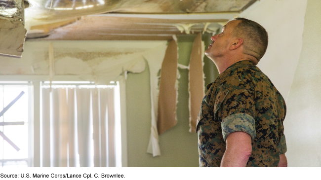 Person in a uniform looking up at a damaged ceiling in a building.