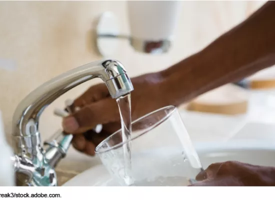 Photo showing someone filling a drinking glass with water from a kitchen faucet.