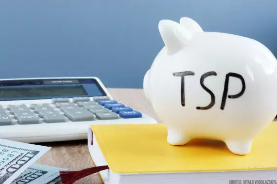 Photo showing a piggy bank with &quot;TSP' written on it in the foreground and a calculator in the background
