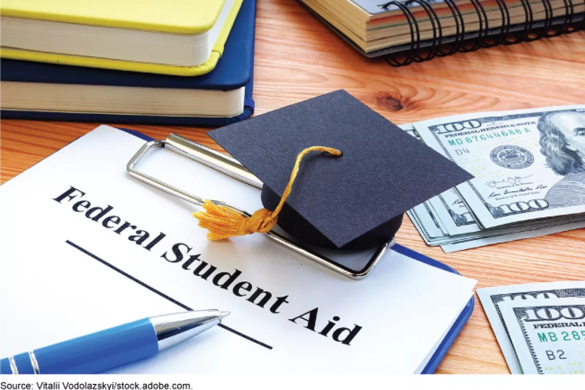 Stock image showing a graduation cap laying on top of a Financial Aid form surrounded by books, notebooks, pens.